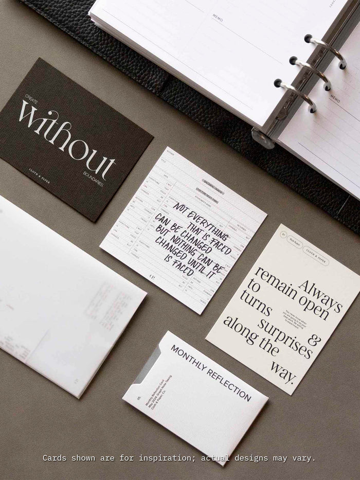 A flat lay of Cloth & Paper’s Assorted Journaling Card Set displayed next to an open planner, featuring neutral-toned cards with motivational quotes and minimalist typography, including cards labeled ‘Monthly Reflection’ and ‘Create without boundaries’.