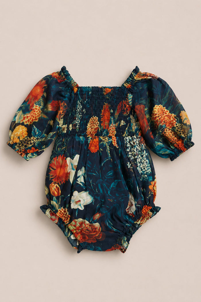 Introducing the Baby Madeline Romper in Imogen Moody Floral by Ivy City Co—a darling chiffon romper adorned with a striking dark floral pattern of red, yellow, and white blooms set against a navy blue backdrop. This charming piece features puffed short sleeves and is beautifully finished with a smocked bodice for enhanced style and comfort.