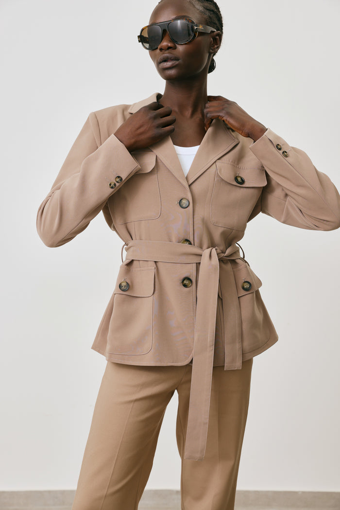 Woman wearing a beige trench coat with a belt against a plain background