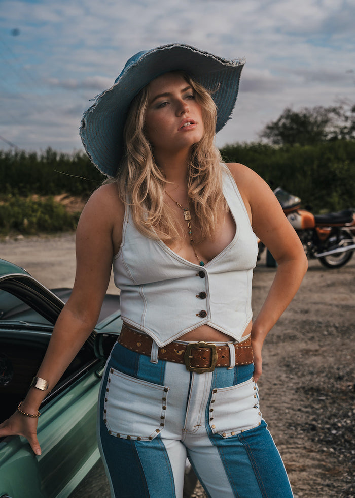 Woman in a white top and blue jeans standing next to a green car with a motorcycle in the background wearing Soul Sister since 1969.