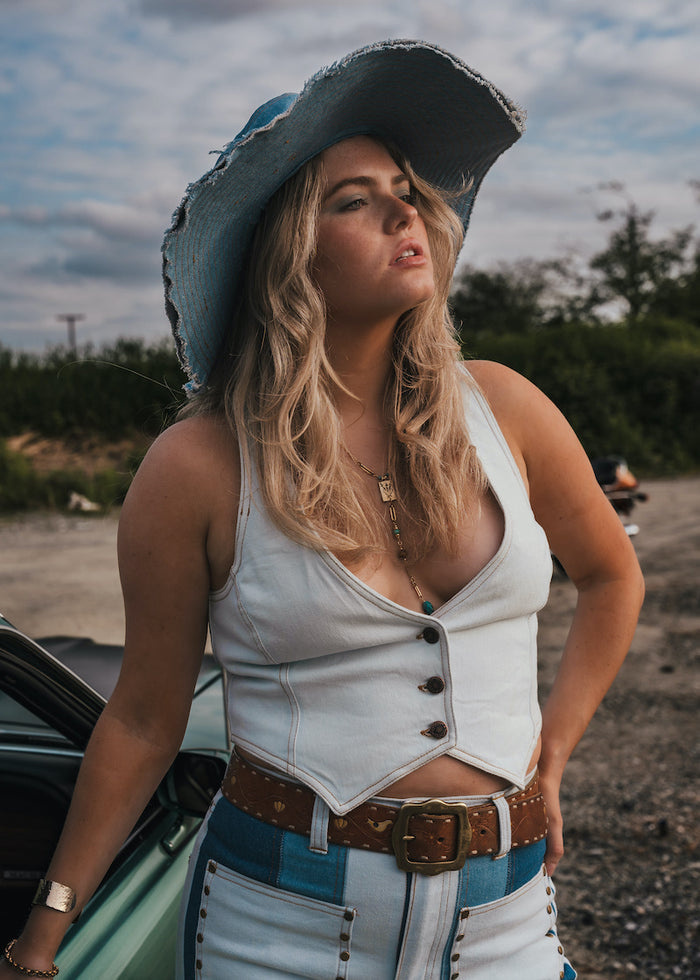 Woman in a white top and blue jeans with a cowboy hat standing next to a car outdoors wearing Soul Sister since 1969..