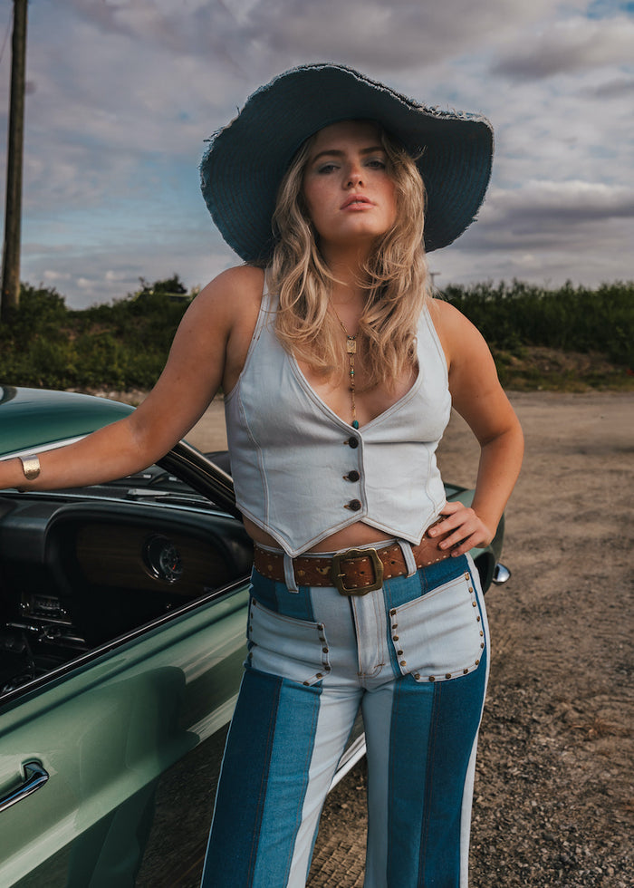Woman in a white top and blue jeans standing next to a green car on a dirt road wearing Soul Sister since 1969..
