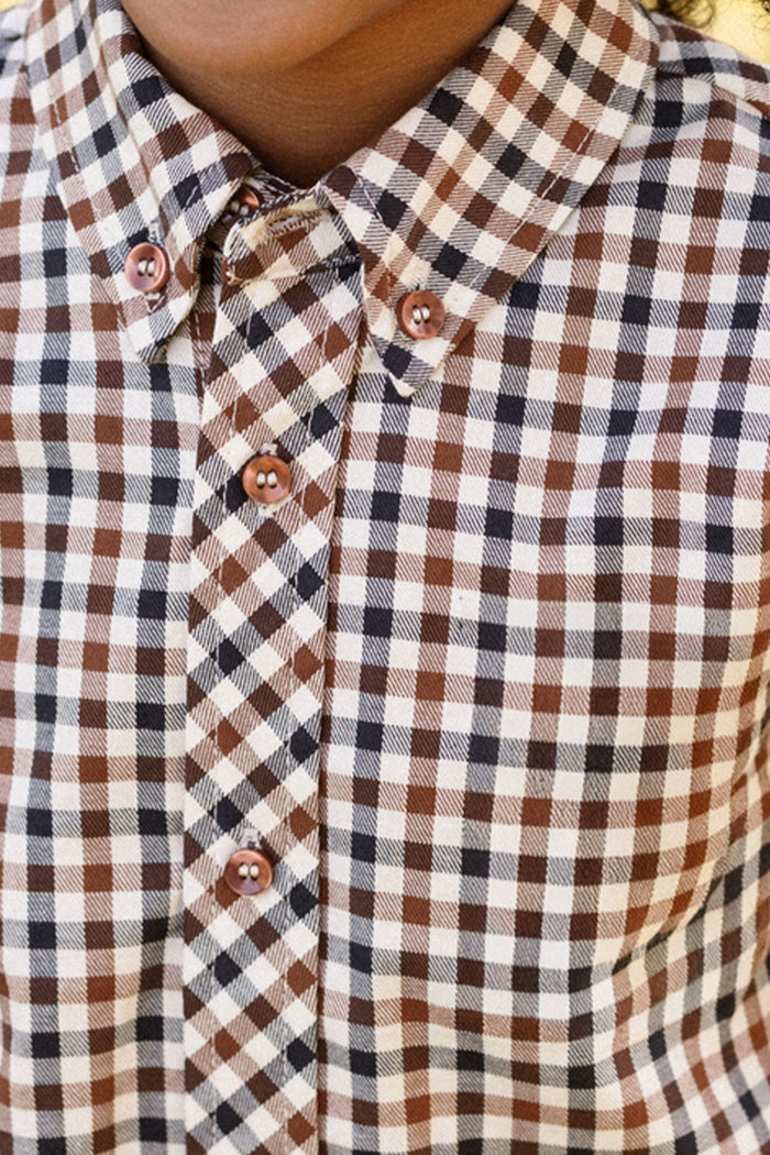 Close-up of the Ivy City Co Boys James Shirt in Chestnut Gingham, featuring brown, black, and white checks buttoned up to the collar. The image highlights the upper chest and neck area, showcasing this stylish boys’ party shirt.