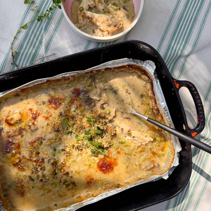 Creamy chicken casserole with peas and herbs, served in foil tray on striped cloth, gluten-free ready meal