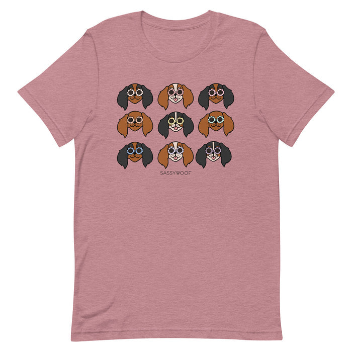 The Cavalier Tee by Sassy Woof is a 100% cotton mauve unisex shirt with nine cartoon dogs in sunglasses and “SASSY WOOF” below—perfect for dog lovers seeking playful, unique style.