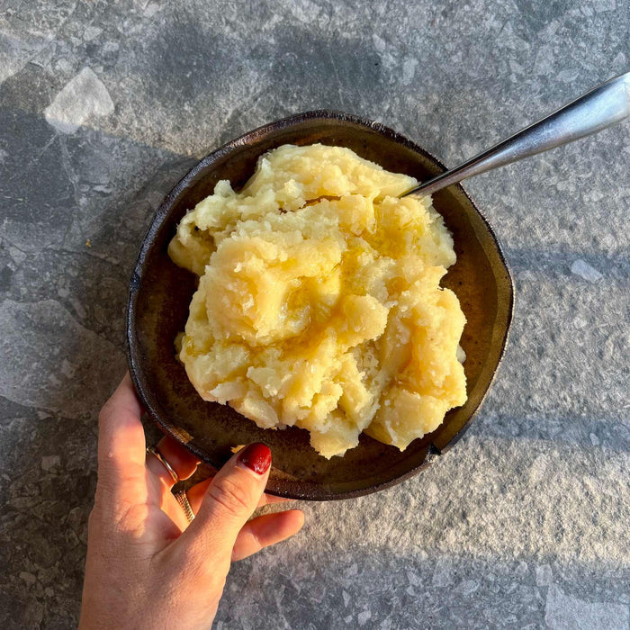 Creamy mashed potatoes in rustic bowl with butter, held over stone surface — organic, gluten-free ready meal