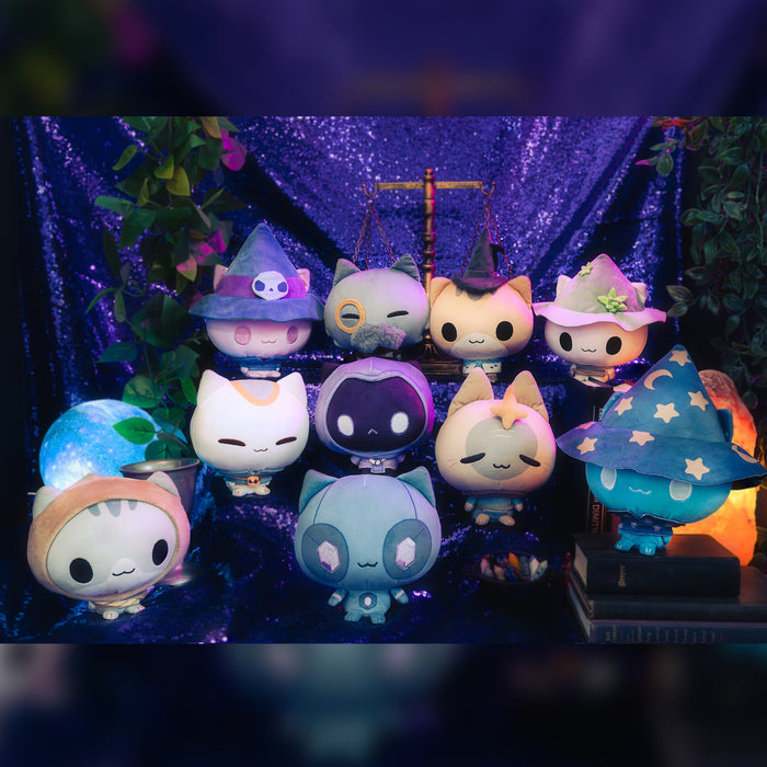 The whole set of 10 Mystic Moon Cloudheads plushies in front of a sparkly purple background. Also visible are books, a salt lamp, a crystal ball, an antique scale and a leafy green plant.