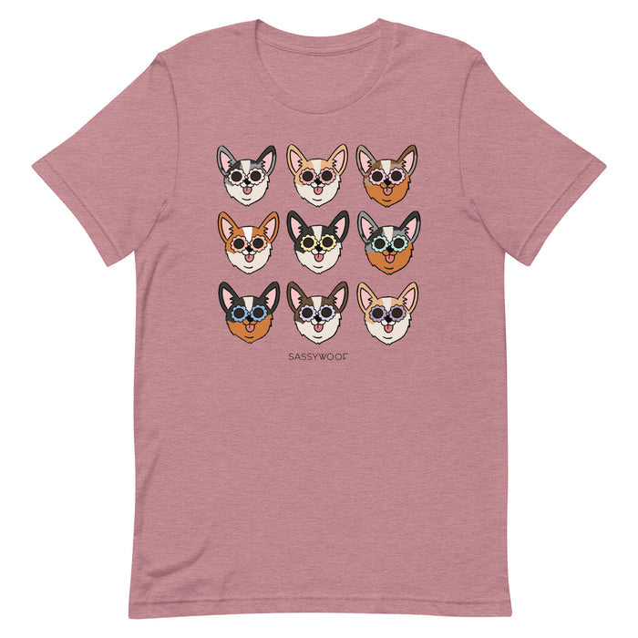 The Corgi Tee by Sassy Woof is a mauve unisex t-shirt with nine illustrated corgi faces in various fur colors and sunglasses above the Sassy Woof logo. Made from 100% cotton for lasting comfort.