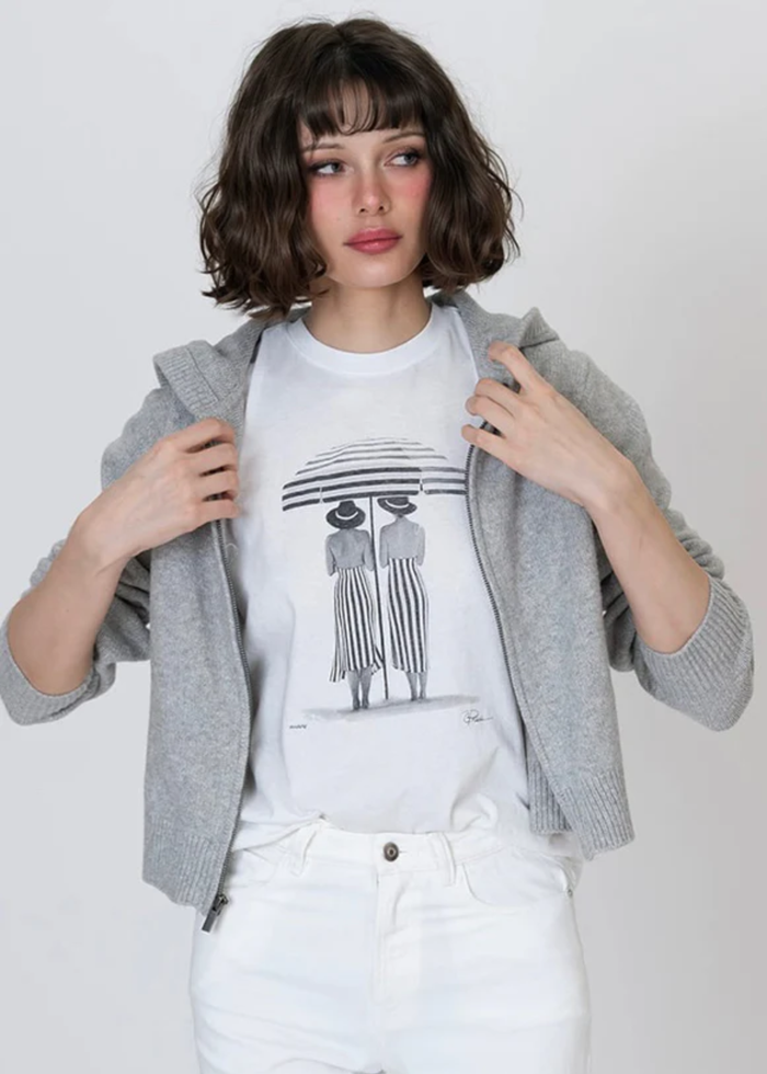 Woman wearing a black and white graphic tee with white jeans and a grey jacket