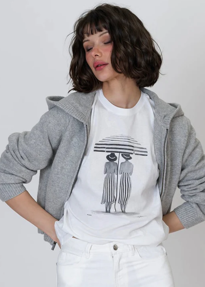Woman wearing a black and white graphic tee with white jeans and a grey jacket