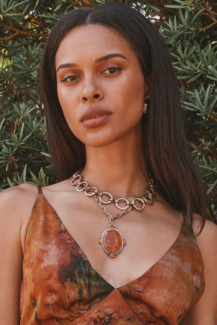 Layered gold chain necklace with oval amber stone pendant worn with a printed slip dress.