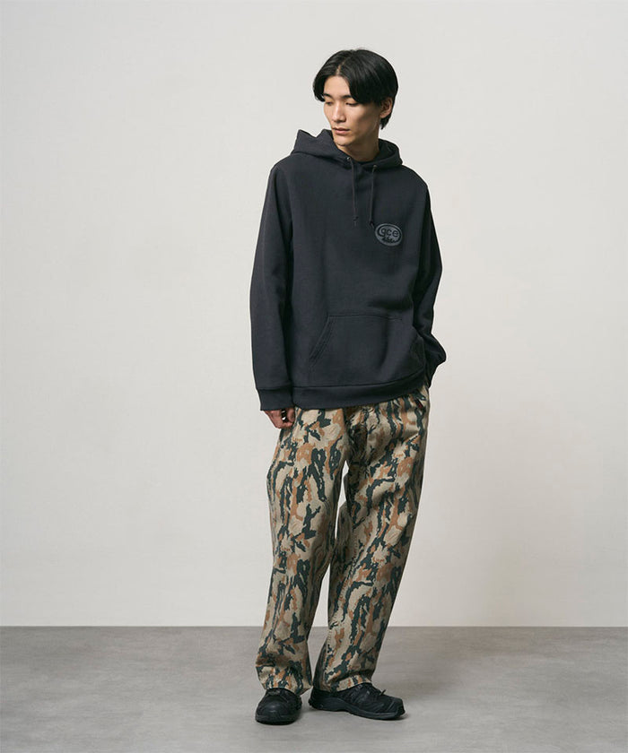 Model wearing bark camo Denim Gramicci Pant Straight Fit and a black hoodie on a light-tone background.