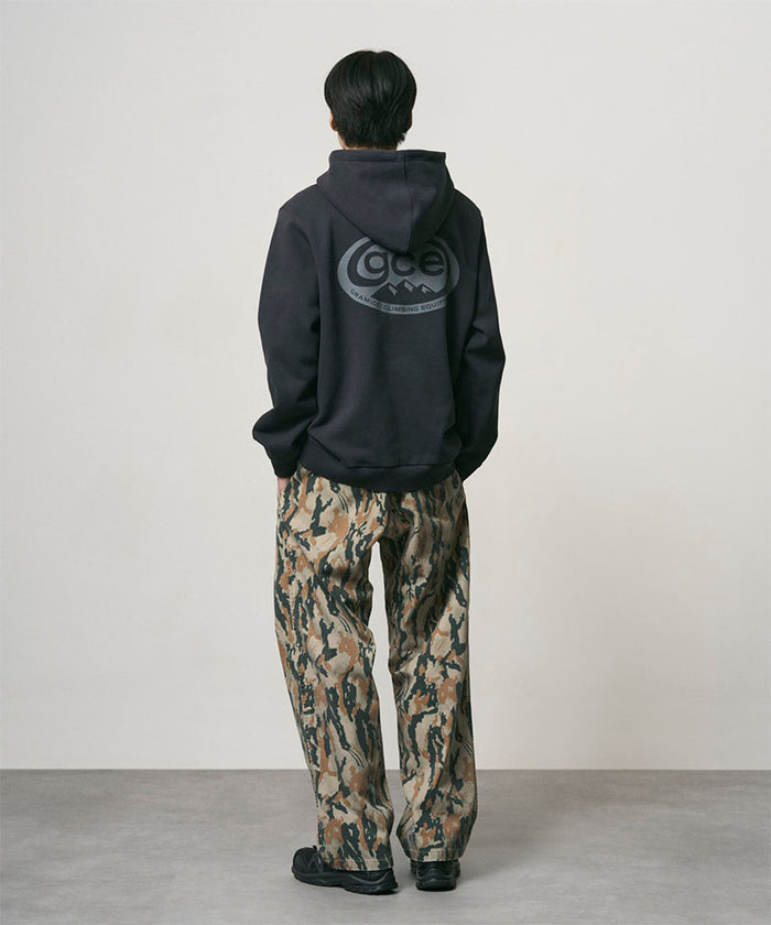 Back view of a model wearing bark camo Denim Gramicci Pant Straight Fit and a black hoodie on a light-tone background.