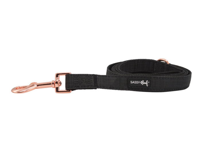 The Sassy Woof Dog Leash - Baby Got Black features a rose gold clasp and signature label, shown coiled on a white background—ideal to pair with a matching black collar or harness.