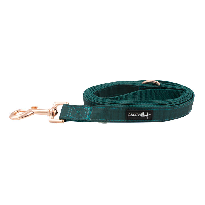 The Sassy Woof Dog Leash - Forest features teal fabric, rose gold hardware, a metal clasp, and the Sassy Woof label. It is coiled neatly on a white background.