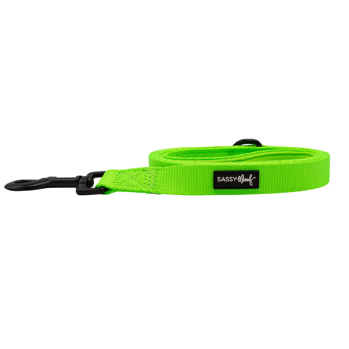 The Sassy Woof Dog Leash - Neon Green features a padded handle with a black label and metal clip, shown coiled on a white background—ideal for those seeking vibrant dog accessories.
