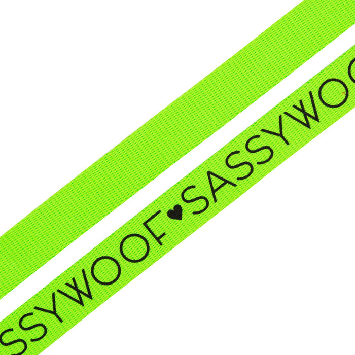The Sassy Woof Dog Leash - Neon Green features a padded handle and black "SASSY WOOF" text with a heart symbol, shown from two angles on a white background. Ideal for anyone seeking vibrant dog accessories.