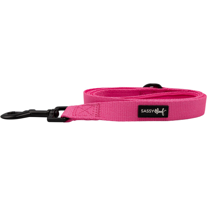 The Sassy Woof Dog Leash - Neon Pink features a black metal clasp and side label, neatly coiled on white—perfect to pair with your favorite adjustable harness or other neon accessories.
