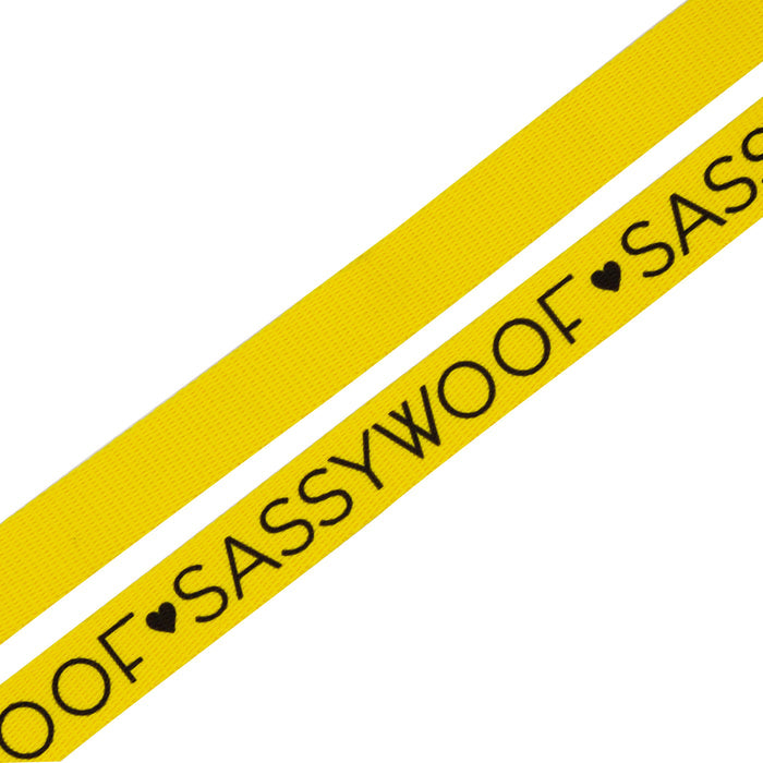 The Dog Leash - Neon Yellow by Sassy Woof features two yellow straps—one plain and one with bold black "SASSY WOOF" text and heart symbols—perfect for pups who love to stand out.