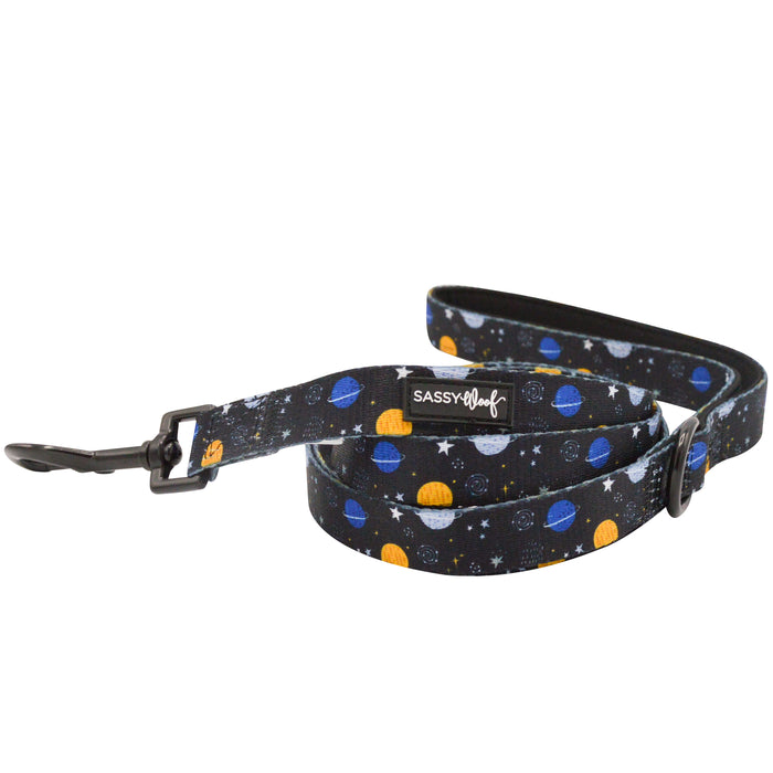 The Sassy Woof "To the Stars and Beyond" dog leash features a space-inspired design with blue, yellow, and white planets and stars, plus a sleek black metal clasp—celebrating girls in STEM and computer science.