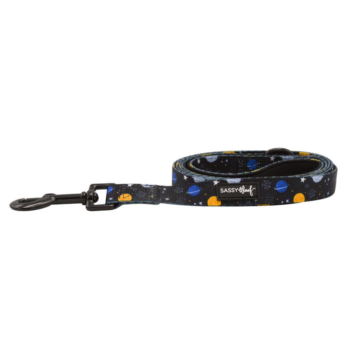 The Sassy Woof Dog Leash - To the Stars and Beyond is a rolled-up leash with a black metal clip, featuring a vibrant, space-themed design of planets and stars on a dark background—perfect for stylish girls in STEM.