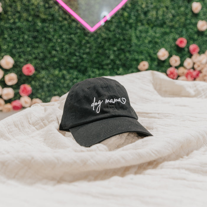 The Sassy Woof Dog Mama Hat - Black features a white heart embroidered on the front. This adjustable cap offers a comfortable fit for dog lovers and fans of chic, casual style.