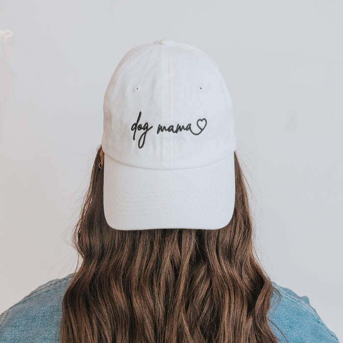 A person with long brown hair wears the Sassy Woof Dog Mama Hat in white, featuring a heart design, photographed from behind against a plain light background.