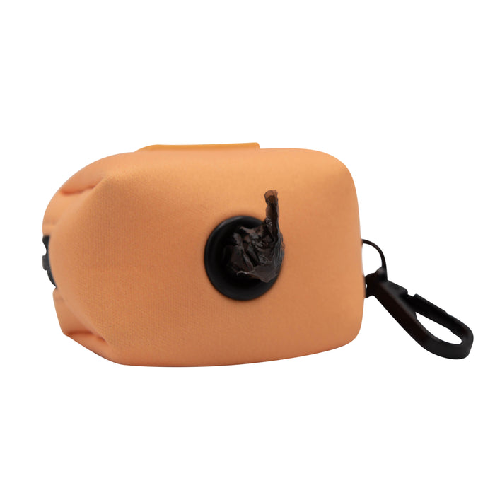The Sassy Woof Dog Waste Bag Holder - Adventure Orange is a peach-toned rectangular holder with a black clip and a bag partially dispensed from its circular opening, shown against a white background.