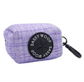 The Sassy Woof Dog Waste Bag Holder - Aurora features a rectangular lavender plaid neoprene design, a black circular dispenser with the brand logo, and a right-side black clip—an ideal stylish accessory for your dog leash.