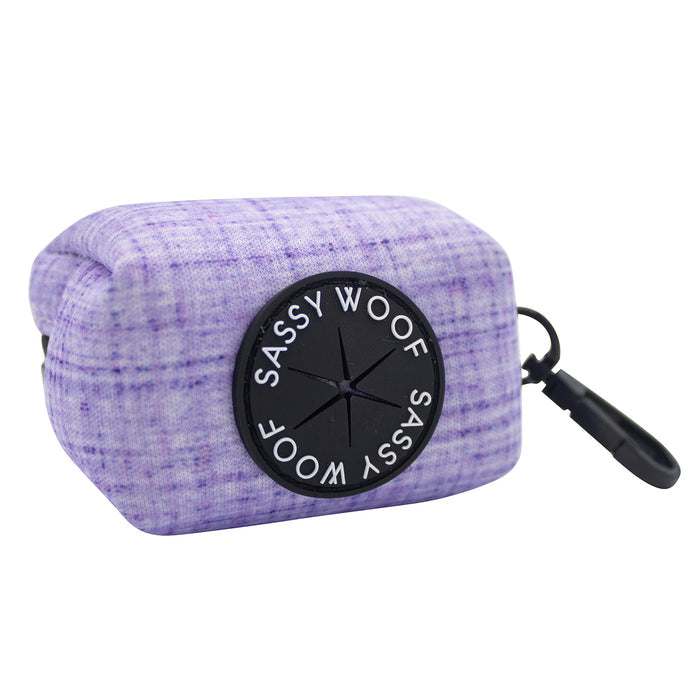 The Sassy Woof Dog Waste Bag Holder - Aurora features a rectangular lavender plaid neoprene design, a black circular dispenser with the brand logo, and a right-side black clip—an ideal stylish accessory for your dog leash.