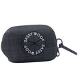 The Sassy Woof Dog Waste Bag Holder - Baby Got Black features a black plaid-patterned neoprene design with a round Sassy Woof logo and a black strap for easy carrying or attachment to dog walking accessories.