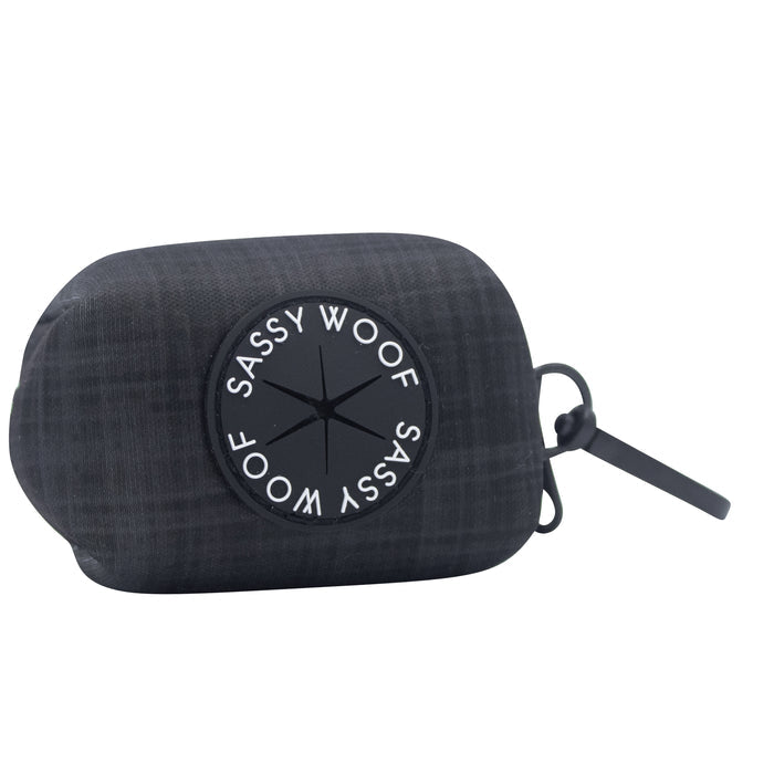The Sassy Woof Dog Waste Bag Holder - Baby Got Black features a black plaid-patterned neoprene design with a round Sassy Woof logo and a black strap for easy carrying or attachment to dog walking accessories.