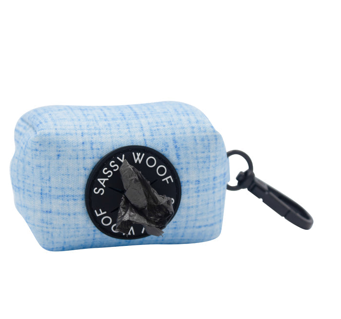 The Dog Waste Bag Holder - Blumond by Sassy Woof is a light blue textured neoprene accessory with a black circular dispenser and clip, featuring a black bag protruding from the opening.