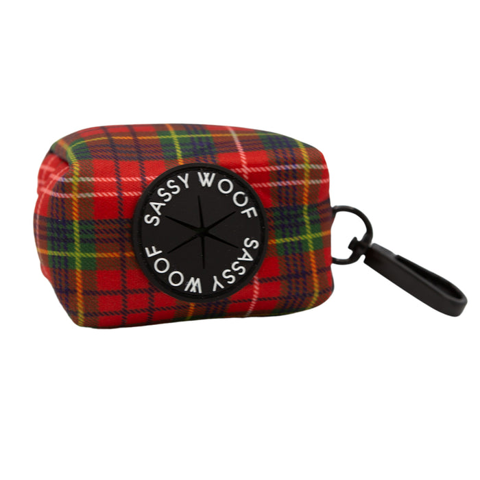The Sassy Woof Dog Waste Bag Holder - Deck the Paws features red and green plaid flannel, a black circular Sassy Woof patch, and a black clip, perfect for carrying your dog's waste bags.