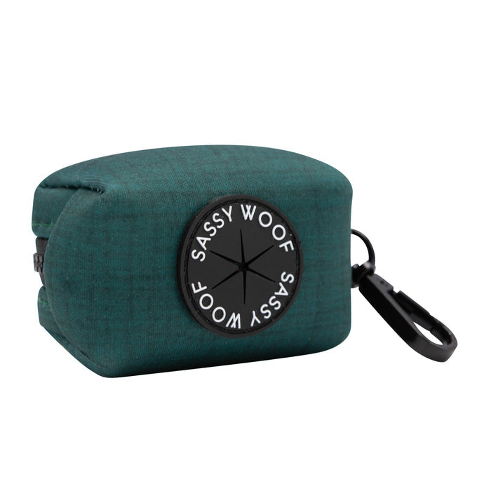 The Sassy Woof Dog Waste Bag Holder - Forest is a green neoprene bag from the Forest Collection with a black circular logo patch and clip for easy attachment to your leash or bag.