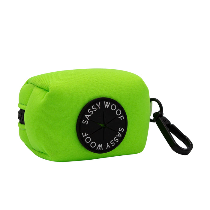 The Sassy Woof Dog Waste Bag Holder - Neon Green is a bright green rectangular neoprene holder with a black circular label and clip, ideal for carrying dog waste bags and pairing with matching neon accessories or harnesses.
