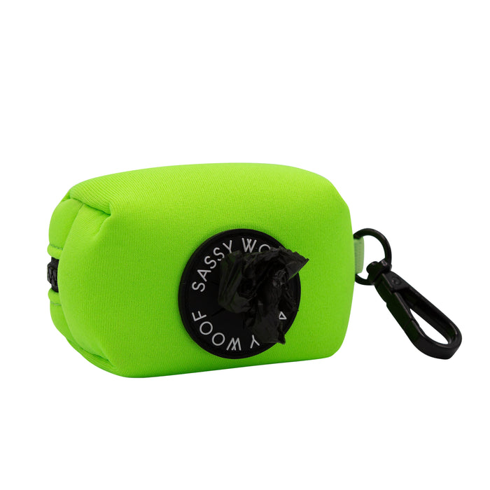 The Sassy Woof Dog Waste Bag Holder in neon green features a black circular opening, secure clip for easy attachment, and pairs perfectly with neon dog accessories or a matching harness.