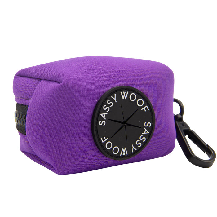 The Sassy Woof Dog Waste Bag Holder in Neon Purple is a small, rectangular neoprene pouch with a zipper, black clip, circular branded patch, and bag-dispensing slit—perfect to complement your colorful dog accessories.