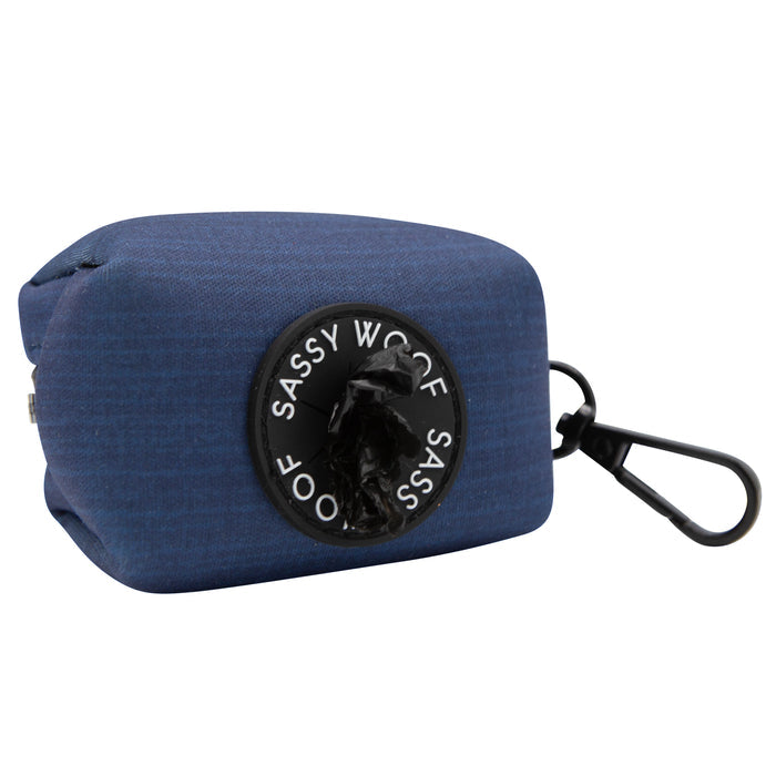 The Sassy Woof Dog Waste Bag Holder - Twilight is a blue neoprene holder with a black brand patch, featuring a clip and dispenser slot. It pairs perfectly with the adjustable harness from the Twilight Collection.