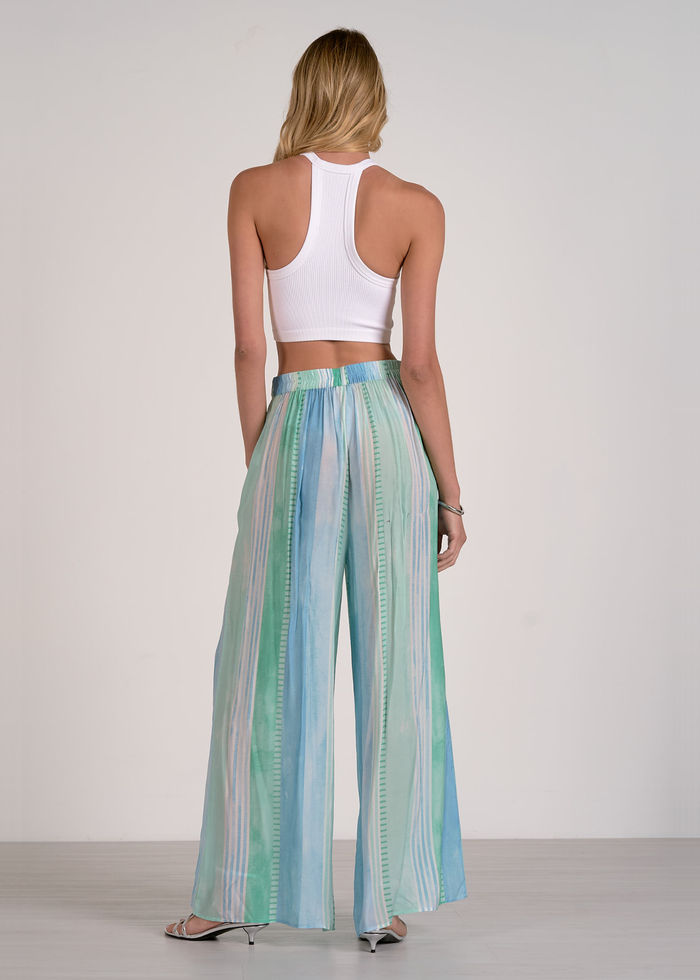 Woman turned around wearing green, blue, and white striped pants with a white crop top and silver heels