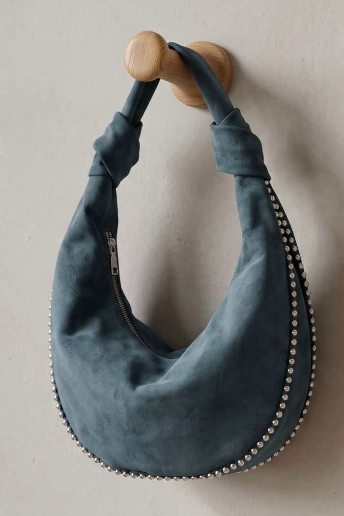 Blue vegan suede crescent hobo bag with silver metal ball trim, knotted shoulder strap, and zip-top closure.
