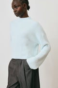 Person wearing a light blue sweater and dark gray pants against a plain background
