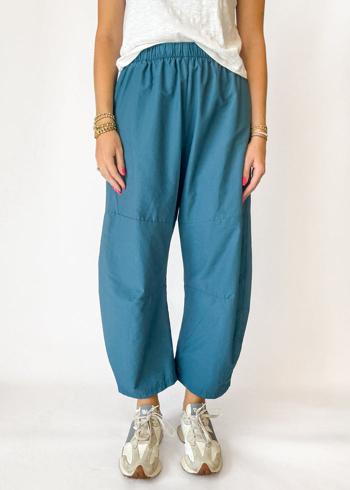 Person wearing teal pants and white sneakers on a plain background