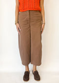 Person wearing brown wide-leg pants with an orange top on a white background