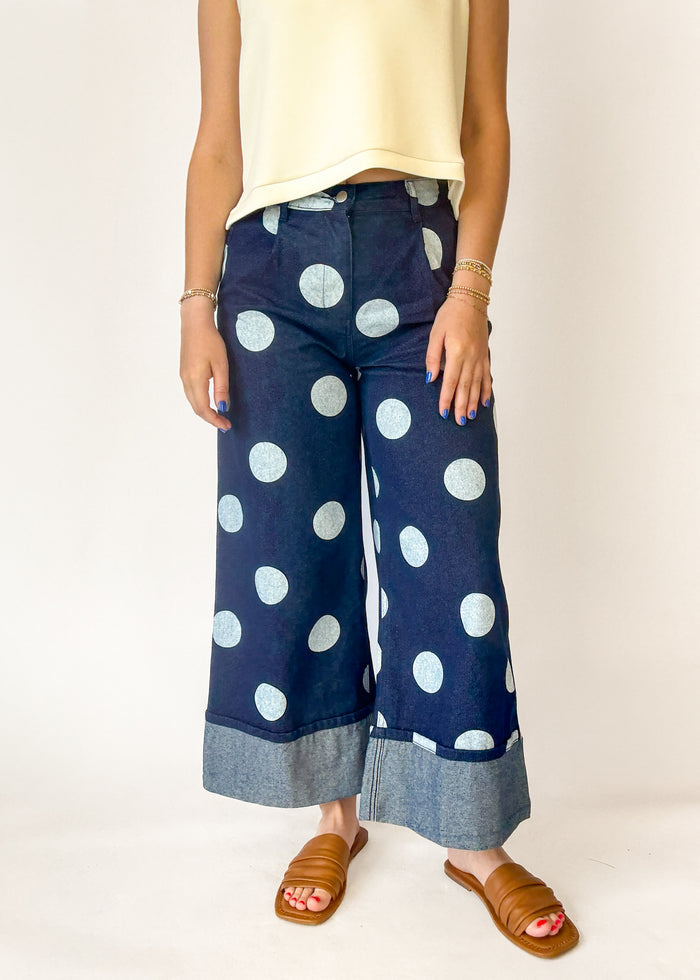 Navy blue pants with white polka dots worn by a person on a plain background