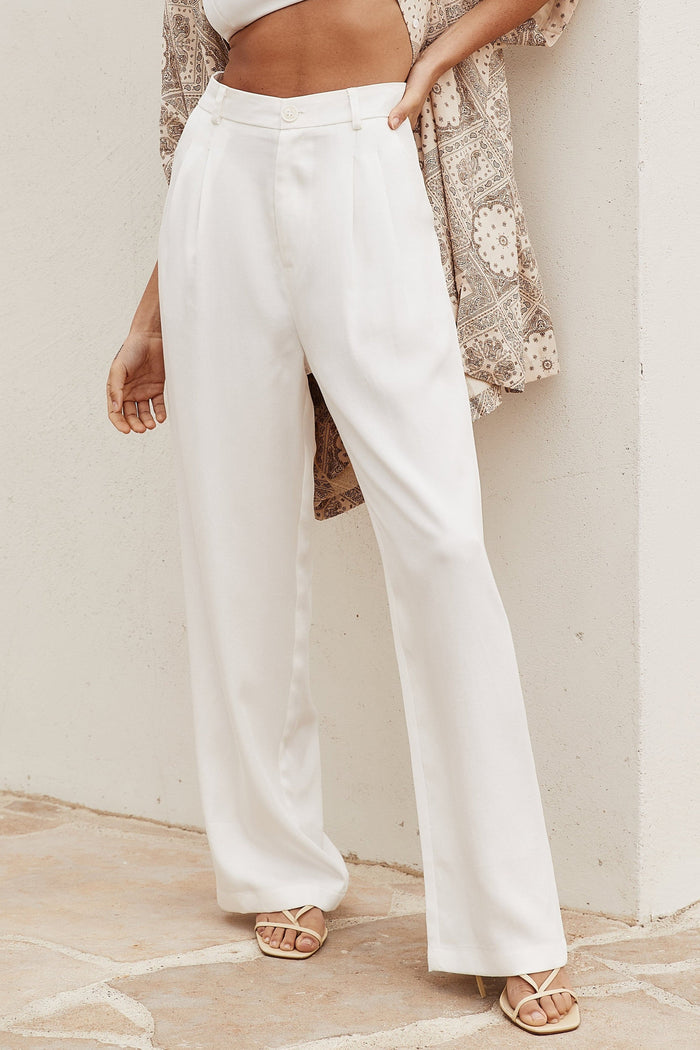Cropped view of white pleated wide leg trousers styled with paisley shirt and strappy sandals.