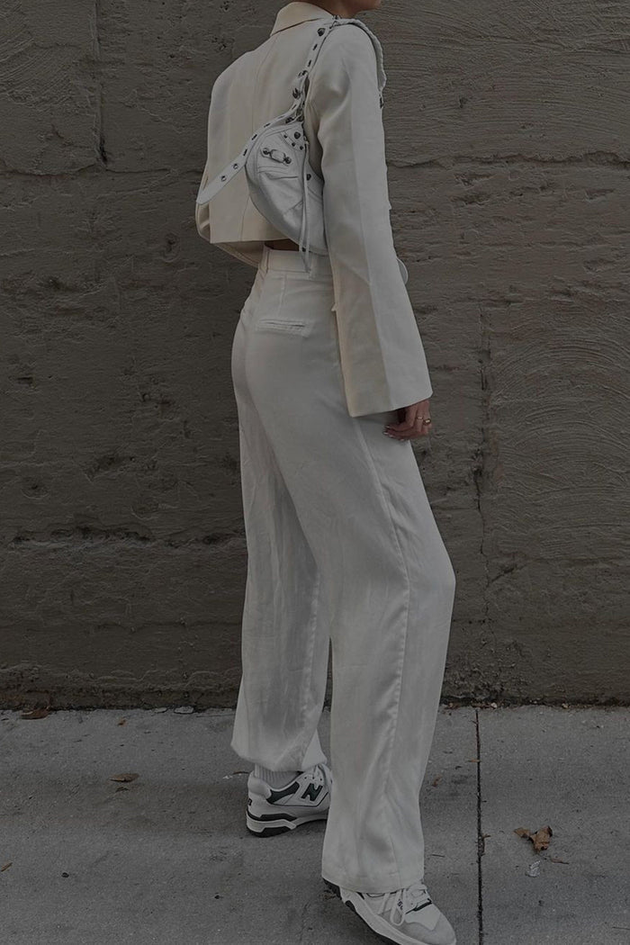 Side view of white wide leg trousers styled with a cropped blazer and sneakers.