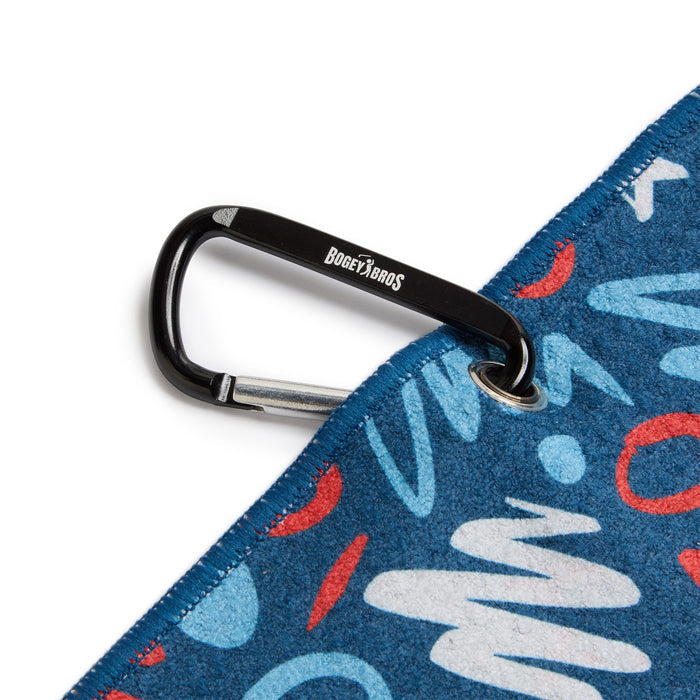 A black carabiner labeled BOGEY BROS clips through a metal grommet on the corner of a blue fabric with a red, white, and light blue abstract pattern and visible stitching on the edge.