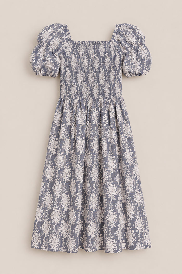 Lisa Dress in Jolie Fleur by Ivy City Co: Blue midi dress with a white floral print, puffed short sleeves, a square neckline, and a smocked bodice with a gathered waist for a flattering fit. Maternity friendly. Displayed on a neutral background.
