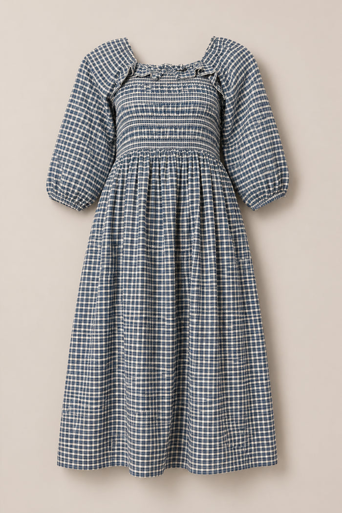 The Mae 3/4 Sleeves Dress in Prussian Blue Plaid by Ivy City Co features a blue and white plaid pattern, puffed 3/4 sleeves, a square neckline, and a smocked fitted bodice. With its gathered skirt that flows to mid-calf, this dress offers a comfortable, maternity-friendly silhouette. Displayed against a plain light background.